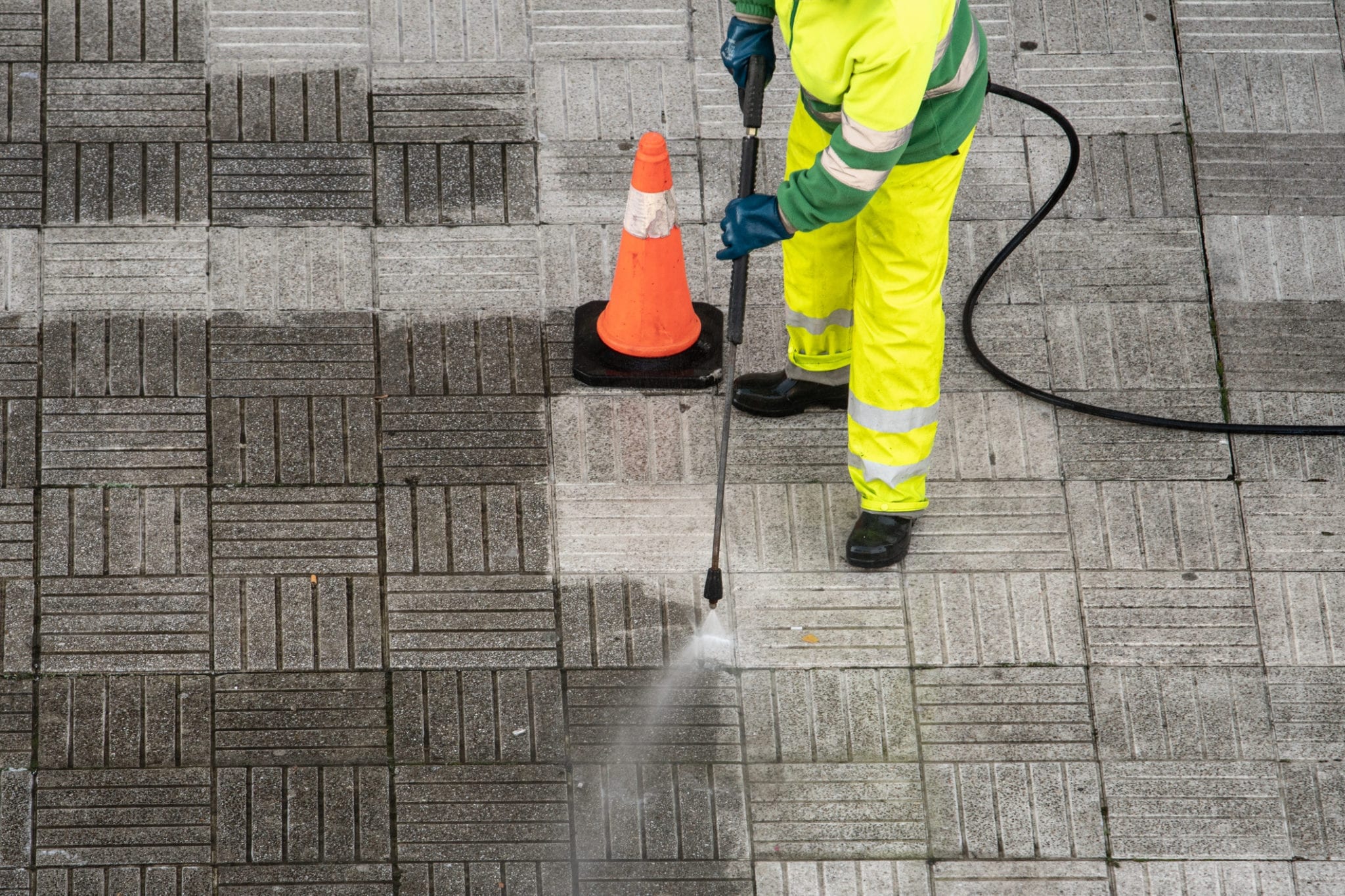 Man in high vis uniform with a power washer, spraying flag stones